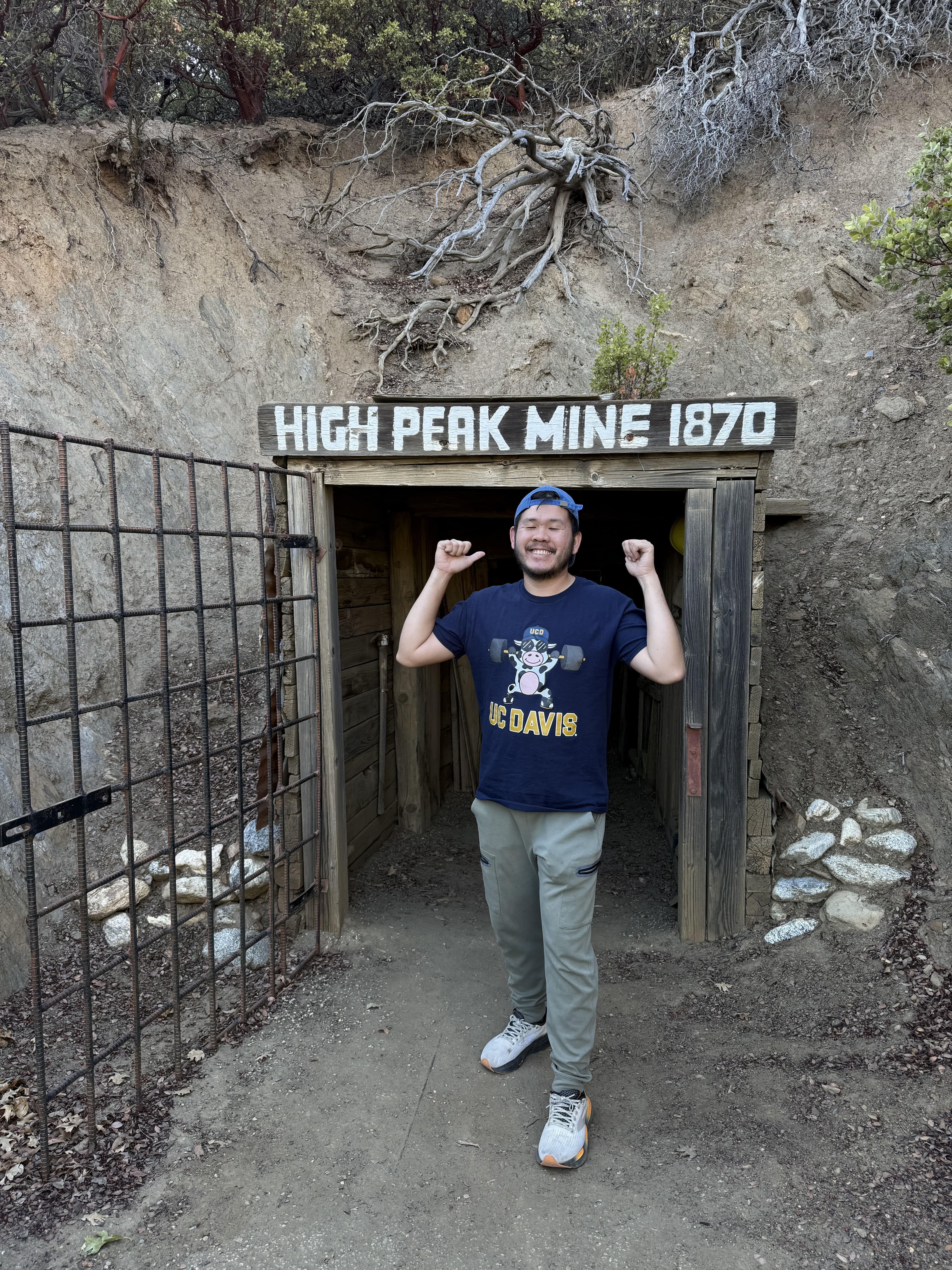 Person smiling at High Peak Mine 1870 entrance, outdoor photo with rocky hillside
